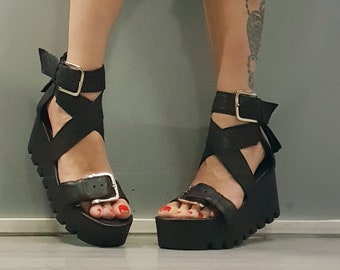 Op de afbeelding: Zwarte platform sandalen met een gespsluiting en gekruiste banden. De sandalen hebben een dikke platform hak en een dikke zool.