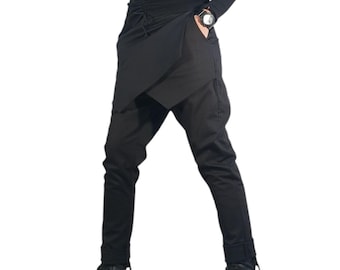 May include: A black long-sleeved turtleneck top worn with black trousers featuring an asymmetrical wrap-style skirt overlay, a drawstring waist, and black leather boots. The outfit is finished with dark sunglasses and a black wristwatch.