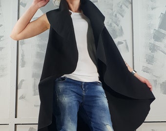 May include: A black sleeveless longline cardigan with a draped collar. The cardigan is worn over a white tank top and blue jeans.