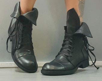 May include: Black leather ankle boots with a unique folded flap design and lace-up closure.