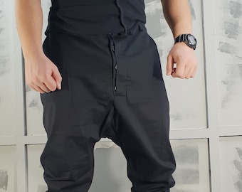 Op de afbeelding: Een zwart T-shirt met een lang, dun banddetail aan de voorkant, gecombineerd met een zwarte, getailleerde broek en zwarte high-top sneakers.