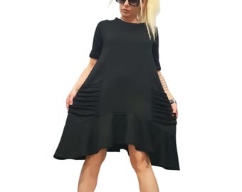May include: A black knee-length dress with short sleeves, a round neckline, and a ruffled hem. The dress features two side pockets with horizontal pleated detailing. The garment is paired with black platform boots featuring white laces and a marbled sole.