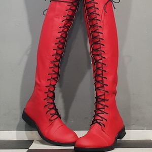 May include: A pair of red knee-high boots with black laces. The boots have a flat sole and a smooth, leather-like texture. The laces run up the front of the boots, creating a striking visual contrast.