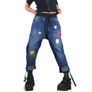 Può includere: Un top nero a maniche corte con cerniera frontale e jeans blu a vita alta con cintura da annodare, orli risvoltati e varie toppe colorate tra cui una stella, un cuore, una faccia che fa l'occhiolino, una lingua rossa e un guanto bianco.