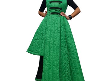 May include: A bright green quilted sleeveless coat featuring a high collar and a series of horizontal black straps across the chest. The garment has an asymmetrical hemline that is shorter on one side and is worn over a black short-sleeved top.