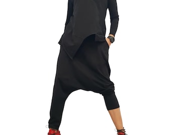 Conjunto de dos piezas negro de vanguardia, top asimétrico con capucha, pantalones de tiro bajo, atuendo gótico.