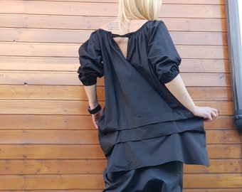 Könnte beinhalten: Eine schwarze, lockere Tunika mit langen Ärmeln und einem Schlüssellochausschnitt im Rücken. Die Tunika wird über einer schwarzen Hose mit weitem Bein und einem gerafften Schritt getragen. Die Person trägt schwarze Stiefeletten mit Schnallen.
