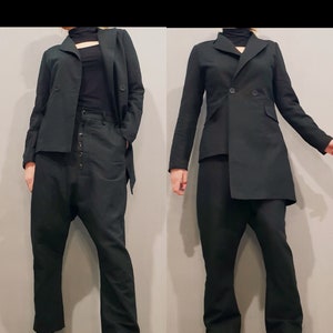 May include: Two black outfits are displayed. The first features a double-breasted blazer, high-waisted pants with button details, and black shoes. The second outfit includes a single-button blazer, matching pants, and black shoes. Both outfits are on a black and white checkered floor.