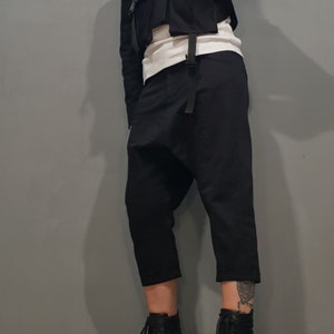 May include: A person wearing black pants with a unique design, a black cropped jacket with pockets and straps, and black lace-up boots with high heels.