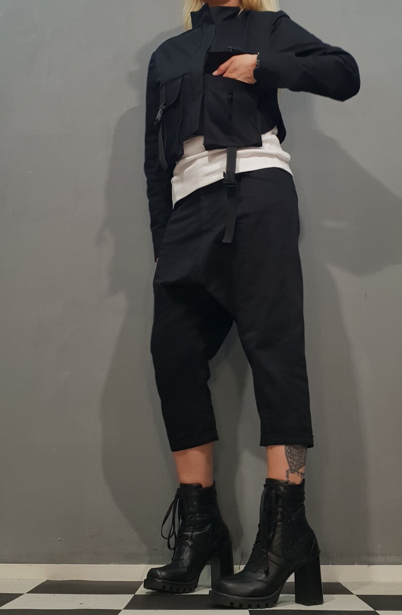 May include: A person wearing black pants with a unique design, a black cropped jacket with pockets and straps, and black lace-up boots with high heels.