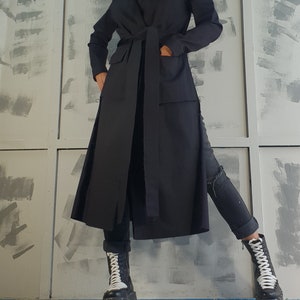May include: A long black coat with a tie belt and pockets. The coat is worn over black jeans and black and white platform boots.
