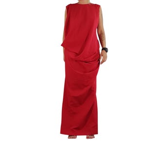 May include: A sleeveless floor-length red dress featuring a high round neckline and a draped fabric design across the bodice and skirt. The garment has a solid red color and a long, flowing silhouette that extends down to the floor.