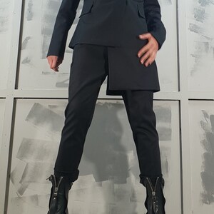 May include: A black blazer with a double-breasted closure and a matching pair of pants. The blazer has a longer back hemline than the front. The person is wearing black heeled boots with zippers.