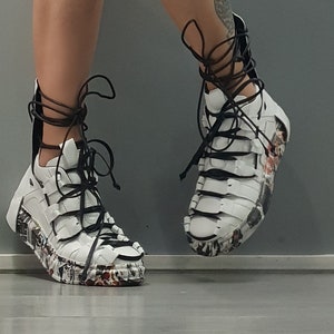 Könnte beinhalten: Weiße High-Top-Sneaker mit schwarzen Schnürsenkeln und einem einzigartigen Design mit einer Mischung aus Texturen und Mustern.
