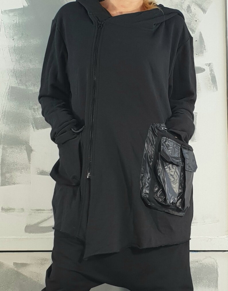 Op de afbeelding: Zwarte hoodie met een lange rits en een groot zwart nylon zakje aan de zijkant.