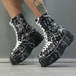 Könnte beinhalten: Schwarz-weiße Plateauschuhe mit weißen Schnürsenkeln und einem weißen Sprühlack-Design. Die Schuhe haben den Text "TURN ON" aufgedruckt.