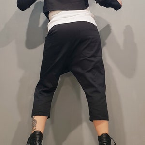 May include: A black cropped jacket with long sleeves and a black pair of cropped pants. The person is wearing black heeled boots.