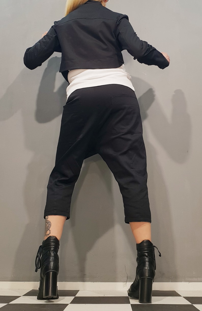 May include: A black cropped jacket with long sleeves and a black pair of cropped pants. The person is wearing black heeled boots.