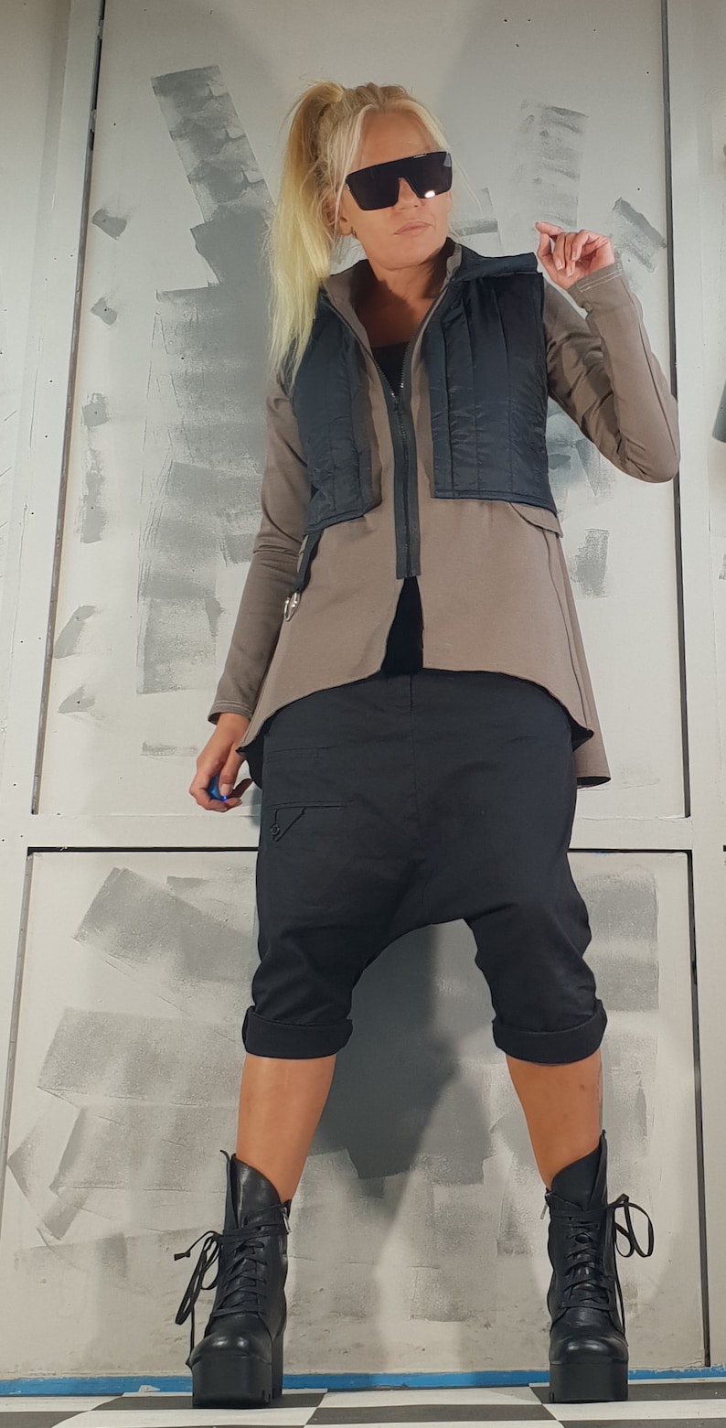 May include: A woman wearing a brown jacket with a black vest, black pants, and black boots. She is wearing sunglasses and has her hair pulled back in a ponytail.