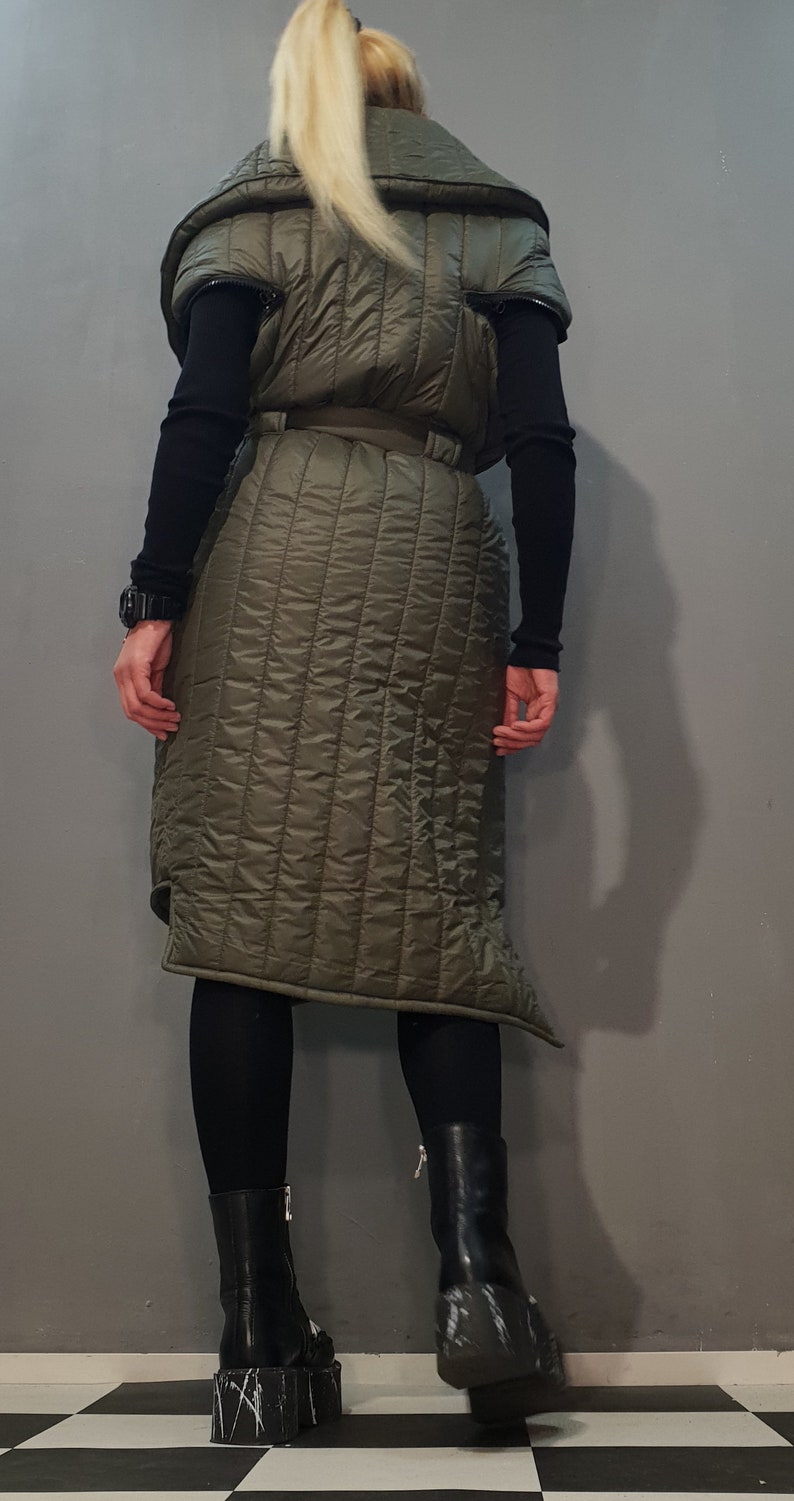 May include: A long, quilted vest with a high collar and a belt. The vest is olive green and has a slightly asymmetrical hemline.