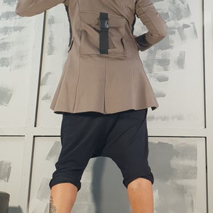 May include: A brown jacket with a black hooded collar and a black strap with a buckle on the back. The jacket has a flared hem and is worn with black pants and black boots.