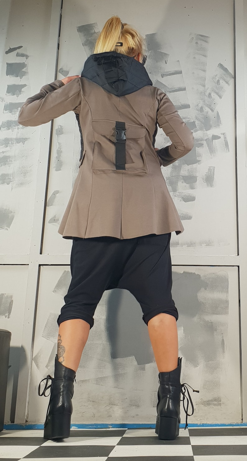 May include: A brown jacket with a black hooded collar and a black strap with a buckle on the back. The jacket has a flared hem and is worn with black pants and black boots.