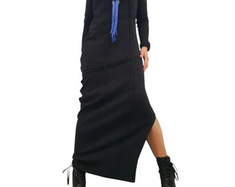 May include: A long-sleeved black maxi dress featuring vertical seam detailing and a side slit, paired with a bright blue cord necklace with a silver ring pendant and black lace-up combat boots with a thick sole and visible stitching.