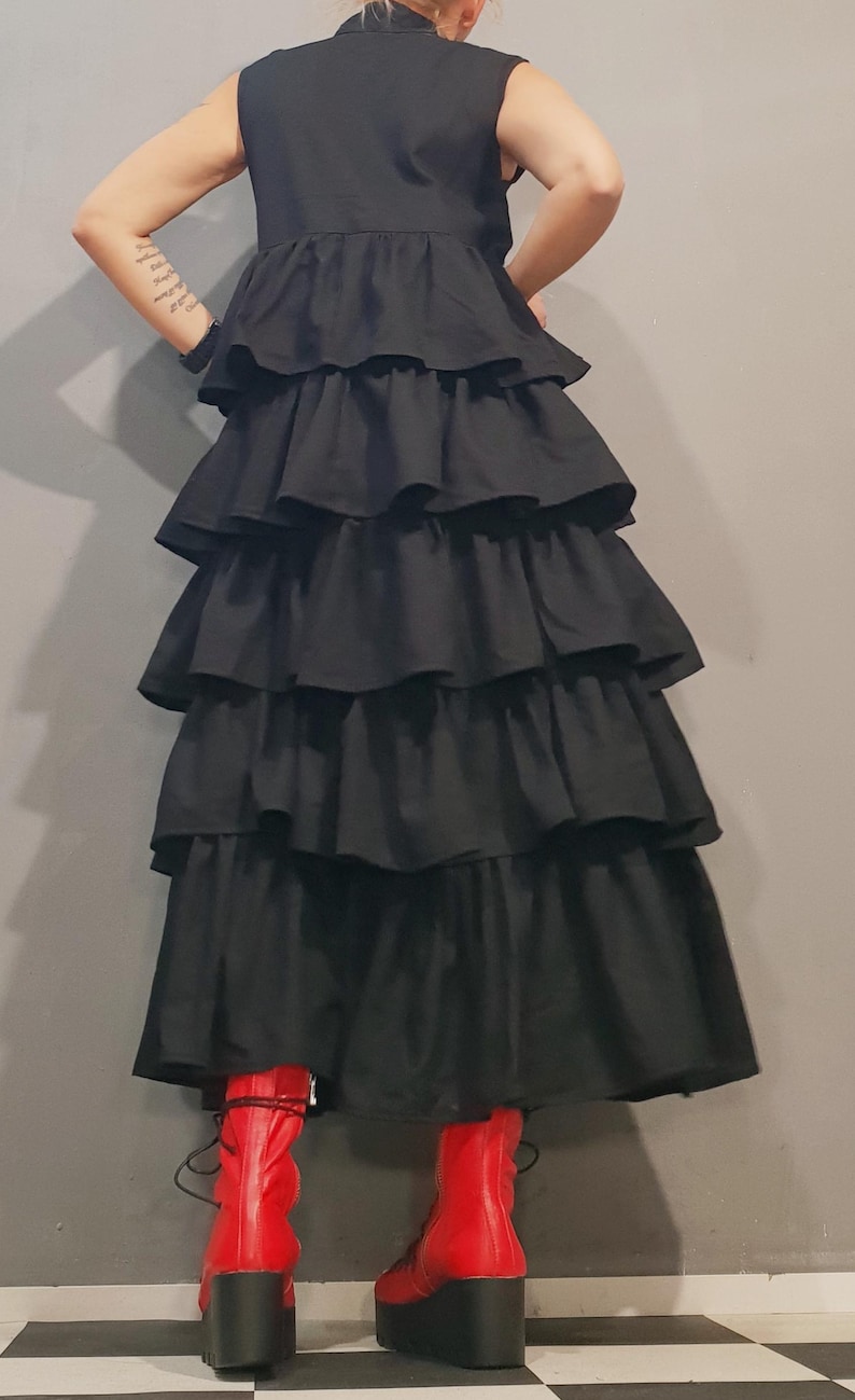 May include: A black sleeveless dress with multiple layers of ruffles. The dress is long and falls to the ankles. The model is wearing red platform boots.