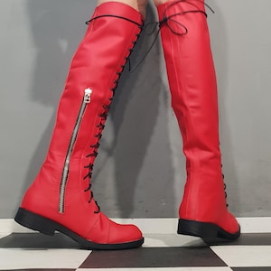 May include: A pair of bright red knee-high boots. The boots feature a lace-up design with black laces, a side zipper, and a black sole. The boots are made of a smooth, shiny material.