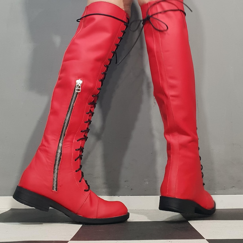 May include: A pair of bright red knee-high boots. The boots feature a lace-up design with black laces, a side zipper, and a black sole. The boots are made of a smooth, shiny material.