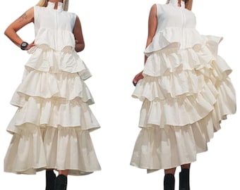 Puede incluir: Vestido blanco sin mangas con cuello alto y falda con volantes escalonados. El vestido tiene cremallera frontal y se combina con botas de plataforma negras. El estilo es moderno y elegante.