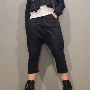 May include: A black cropped jacket with multiple straps and pockets, paired with black cropped pants and black heeled boots.