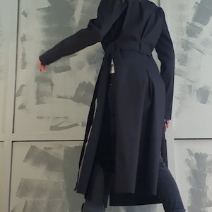 May include: A black long-sleeved coat with a belt and a slit in the back. The coat is worn over dark blue jeans and black platform boots.