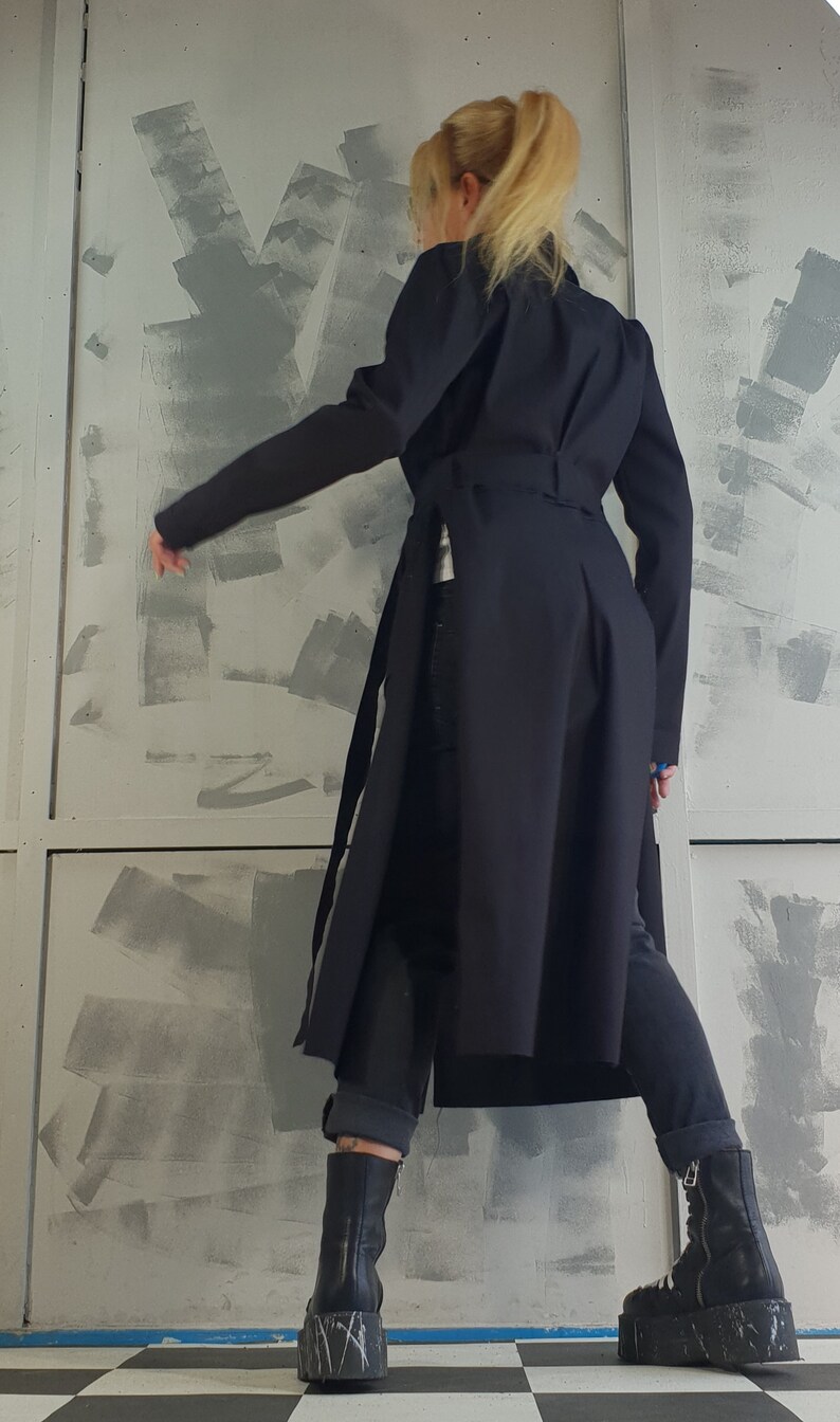 May include: A black long-sleeved coat with a belt and a slit in the back. The coat is worn over dark blue jeans and black platform boots.