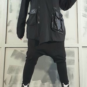 Op de afbeelding: Een zwarte hoodie met een rits en een grote zwarte zak aan de rechterkant. De jas wordt gedragen over een zwarte broek en witte platformlaarzen.