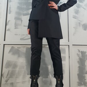 May include: A black blazer with a double-breasted closure and a long, asymmetrical hemline. The blazer is paired with black pants and black heeled boots with zippers.