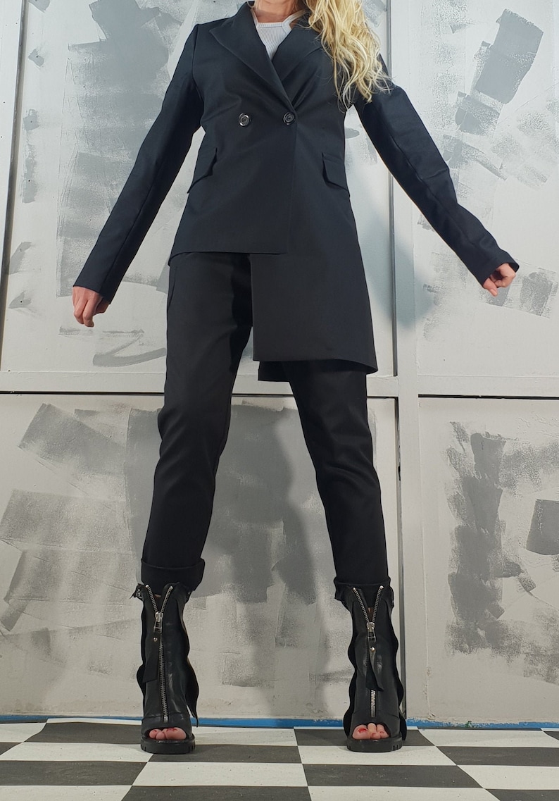 May include: A black blazer with a long, asymmetrical hemline, worn with black pants and black heeled boots with zipper accents.
