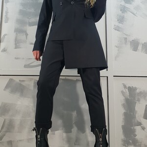 May include: A black blazer with a double-breasted closure and a long, asymmetrical hemline. The blazer is paired with black pants and black heeled boots with a zipper detail.