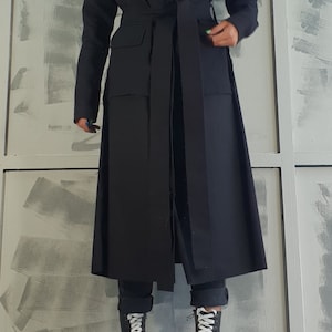 May include: A long black belted coat with a wide collar and pockets. The coat is worn over black pants and black and white platform boots.
