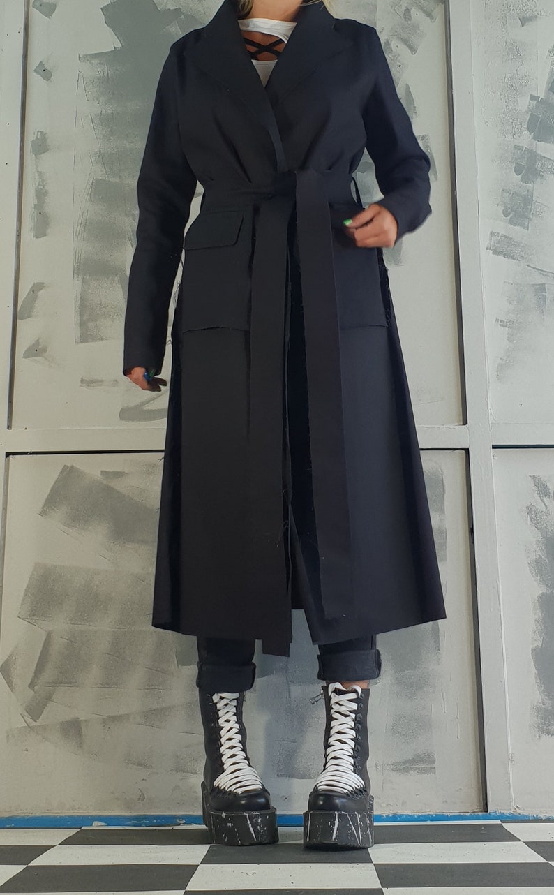 May include: A long black belted coat with a wide collar and pockets. The coat is worn over black pants and black and white platform boots.