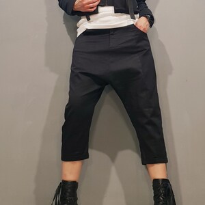 May include: A black cropped jacket with multiple pockets and buckles, paired with black cropped pants and black lace-up boots.