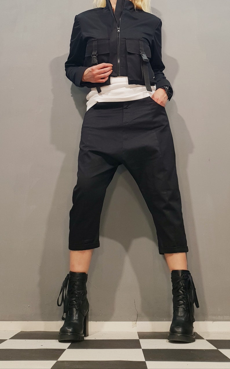 May include: A black cropped jacket with multiple pockets and buckles, paired with black cropped pants and black lace-up boots.