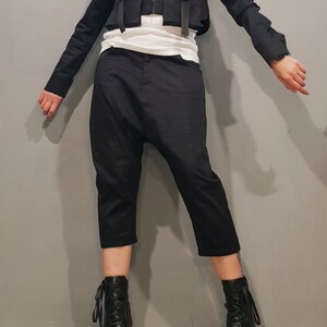 May include: A black cropped jacket with multiple pockets and buckles, paired with black cropped pants and black lace-up boots.