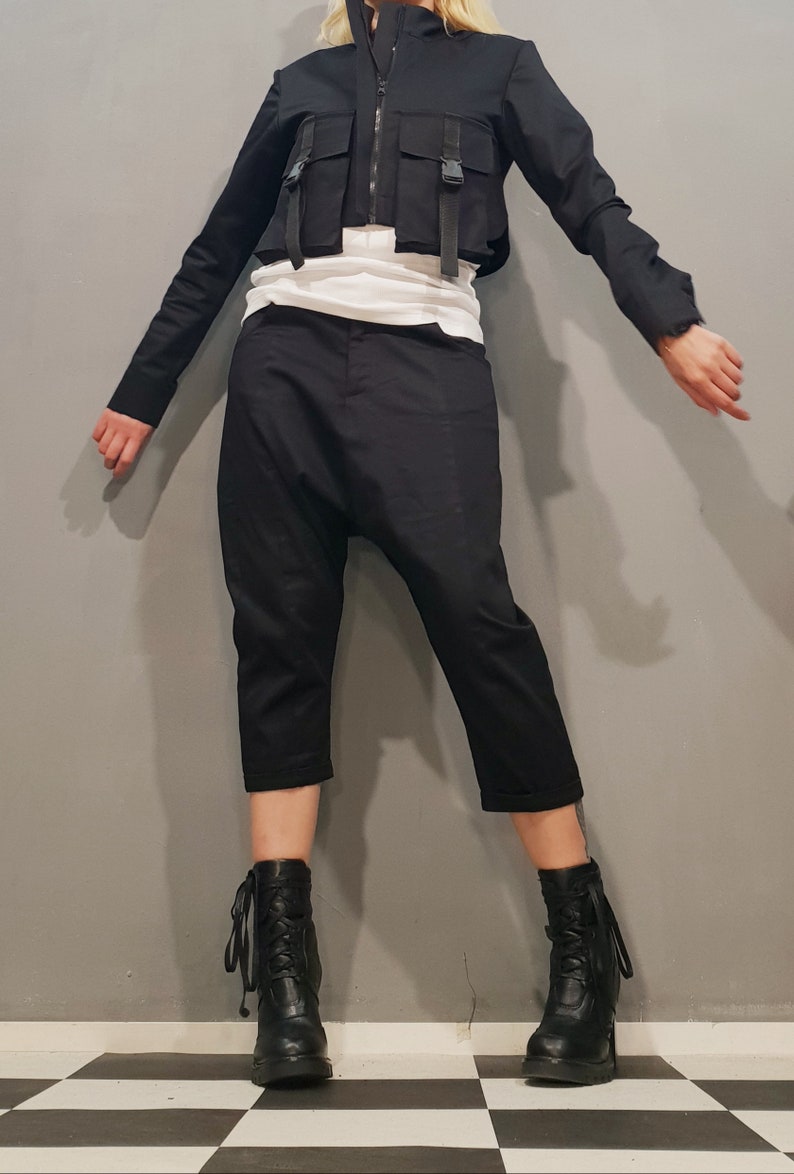 May include: A black cropped jacket with multiple pockets and buckles, paired with black cropped pants and black lace-up boots.