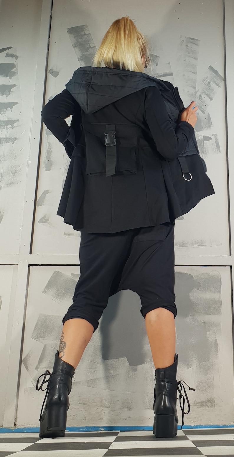 May include: A black hooded jacket with a zipper closure and a belt. The jacket has a quilted lining and a large pocket on the back. The model is wearing black pants and black boots.