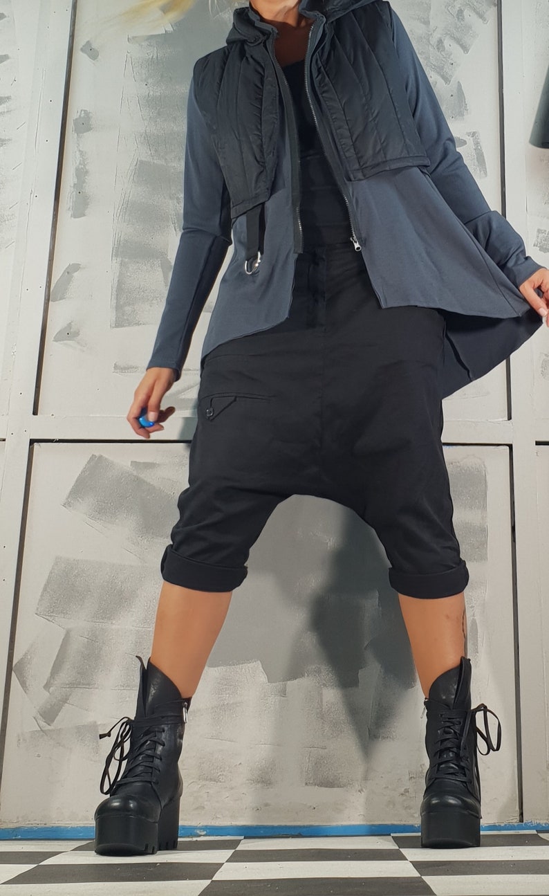 May include: A person wearing a black quilted vest over a gray long-sleeved shirt and black pants. The pants have a unique design with a gathered crotch and cuffed legs. The person is wearing black lace-up boots with thick soles.