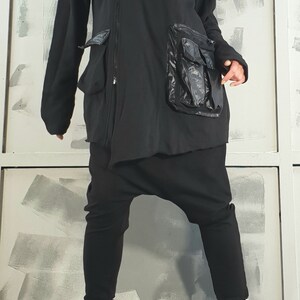 Op de afbeelding: Zwarte hoodie met een rits en een grote zwarte zak aan de voorkant. De jas wordt gedragen over een zwarte broek en zwarte platformlaarzen met witte veters.