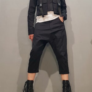 May include: A black cropped jacket with a high collar and multiple straps and pockets. The jacket is paired with black cropped pants and black lace-up boots.