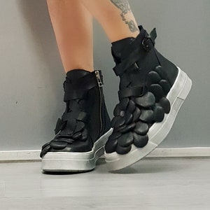 May include: Black leather ankle boots with a unique flower-shaped design on the upper part of the boot. The boots have a white platform sole and a zipper on the side.