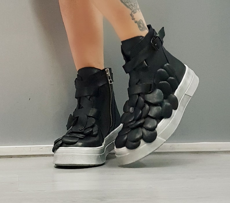 May include: Black leather ankle boots with a unique flower-shaped design on the upper part of the boot. The boots have a white platform sole and a zipper on the side.